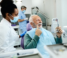 Man in green sweater in dental chair pointing out his teeth to his dentist