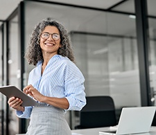 Woman in striped shirt leaning against table smiling holding tablet