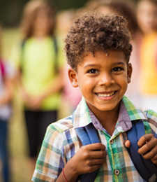 Young boy wearing backpack and smiling at school