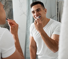 A young man brushing his teeth in front of a bathroom mirror