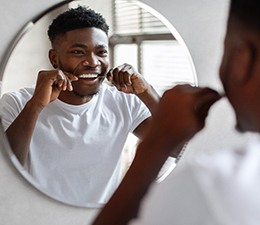 A young man flossing between his teeth in front of a mirror