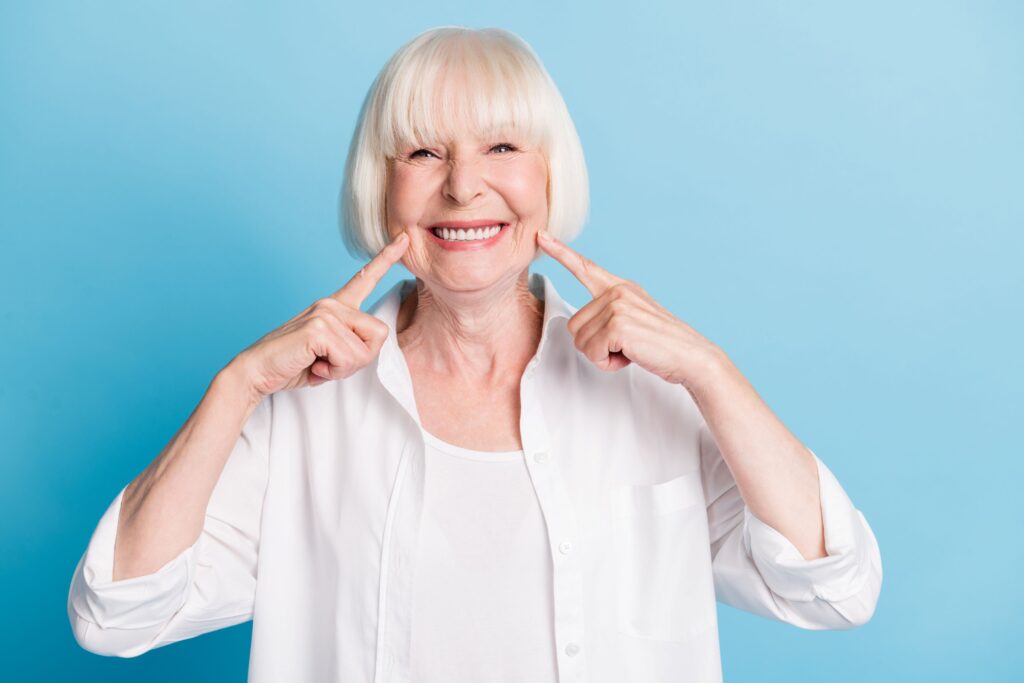 Woman in white shirt pointing to her smile with both hands